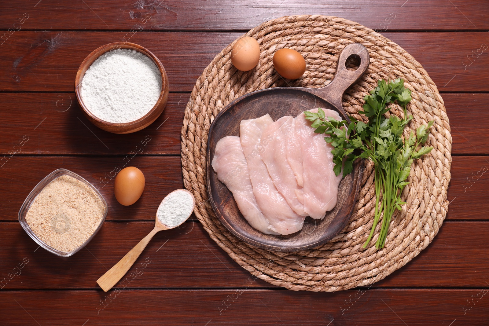 Photo of Making schnitzel. Board with raw meat, parsley and other ingredients on wooden table, flat lay