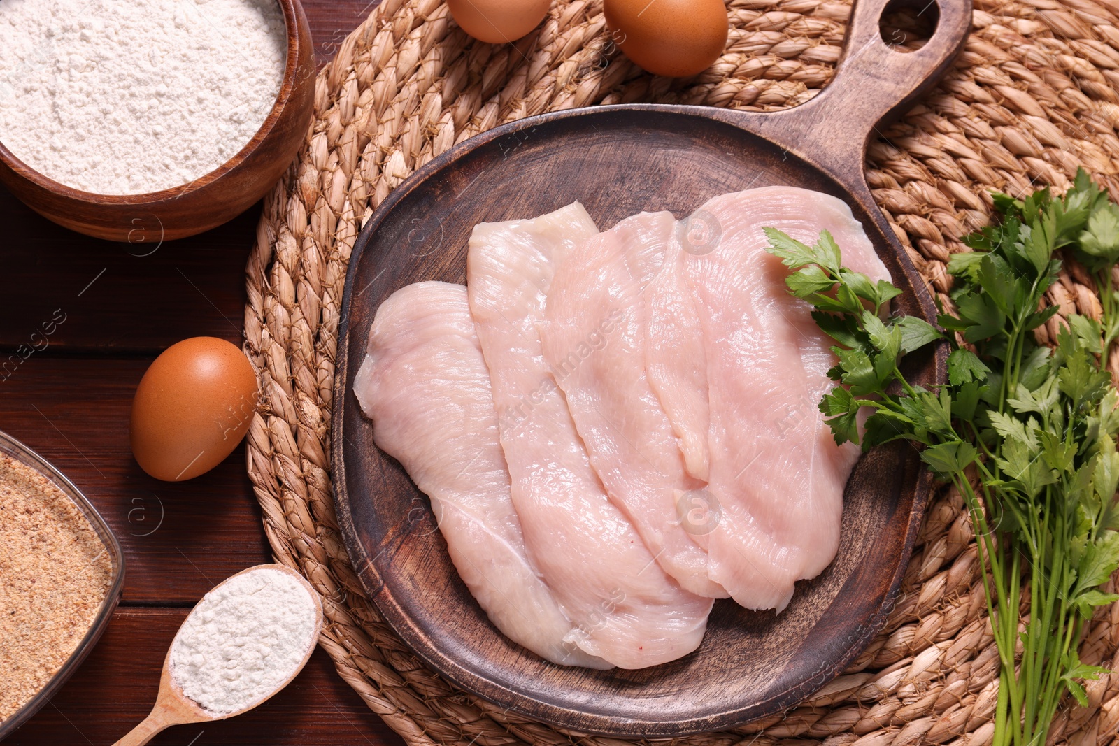 Photo of Making schnitzel. Board with raw meat, parsley and other ingredients on wooden table, flat lay