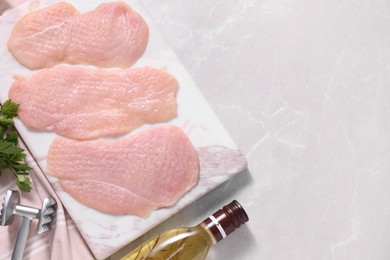 Making schnitzel. Raw meat chops, parsley, oil and tenderizer on light marble table, flat lay. Space for text