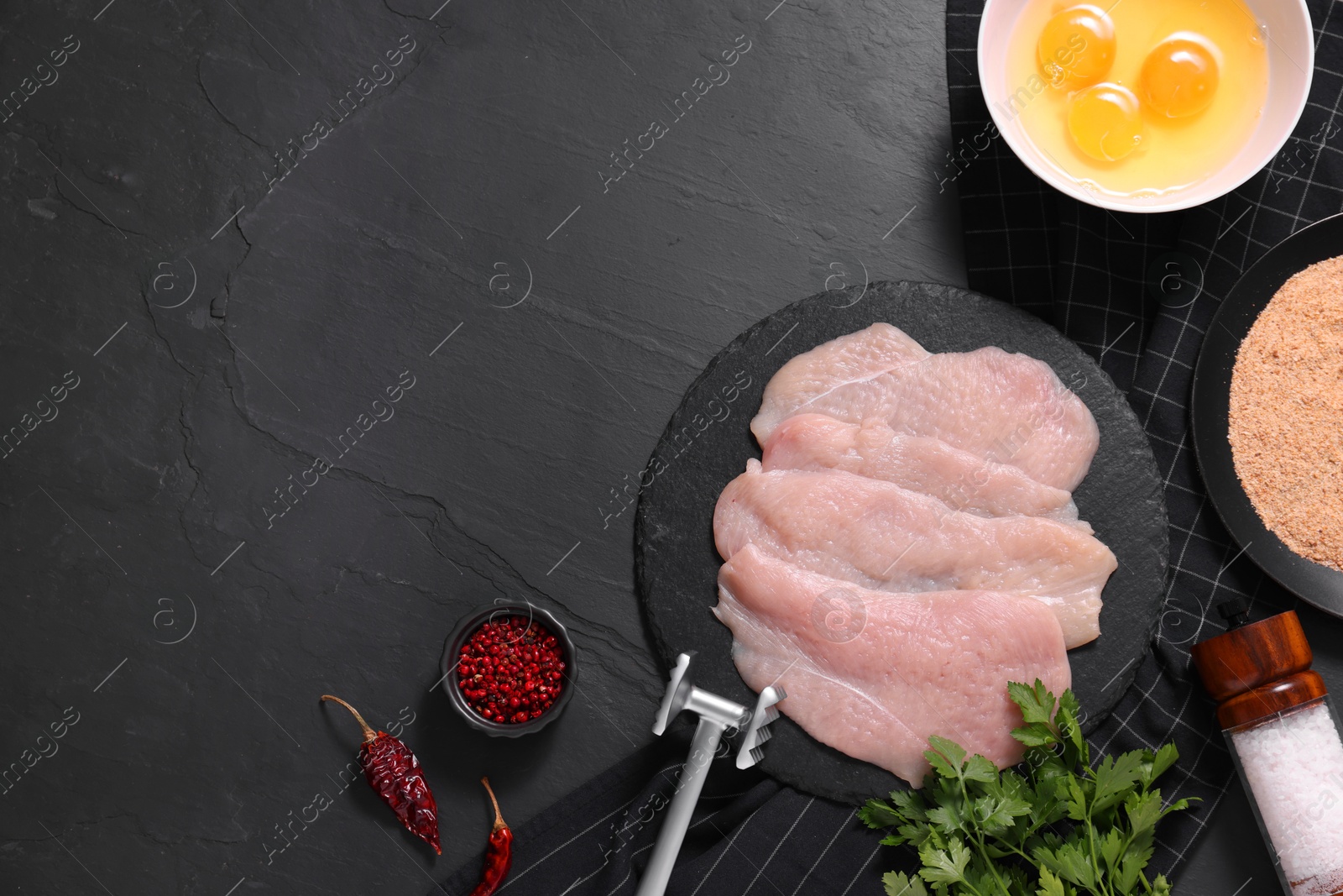 Photo of Making schnitzel. Raw meat chops, products and tenderizer on dark textured table, flat lay. Space for text