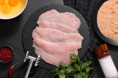 Photo of Making schnitzel. Raw meat chops, products and tenderizer on dark textured table, flat lay