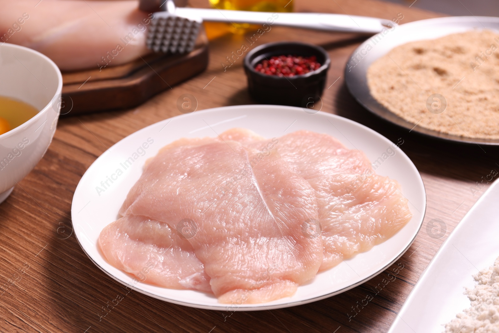 Photo of Making schnitzel. Plate with raw meat on wooden table, closeup