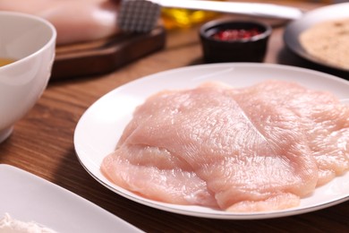 Photo of Making schnitzel. Plate with raw meat on wooden table, closeup