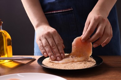 Photo of Making schnitzel. Woman coating slice of meat with bread crumbs at wooden table, closeup