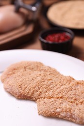 Making schnitzel. Plate with raw slice of meat in bread crumbs on wooden table, closeup