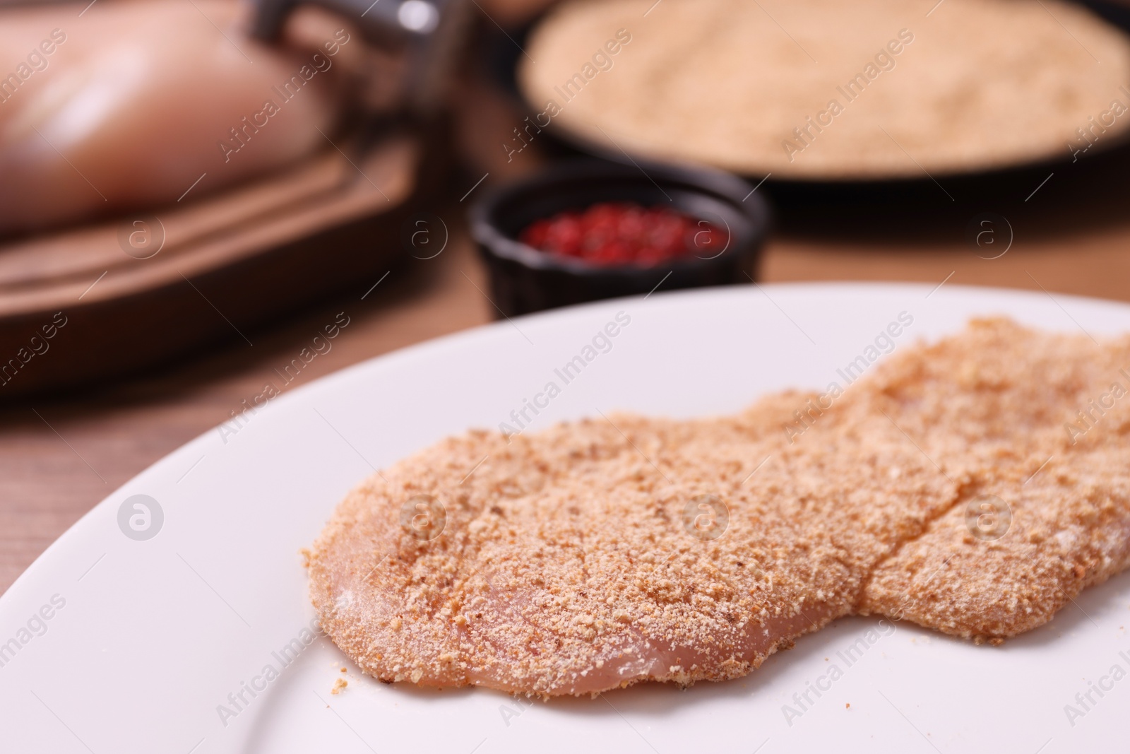 Photo of Making schnitzel. Plate with raw slice of meat in bread crumbs on wooden table, closeup