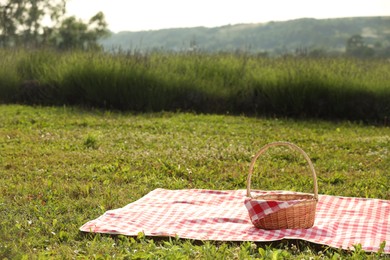 Photo of Picnic wicker basket with napkin and red checkered blanket on green grass outdoors