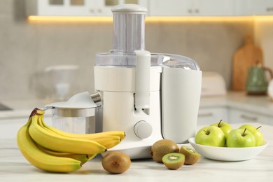 Photo of Modern juicer, apples, kiwi and bananas on white marble table in kitchen