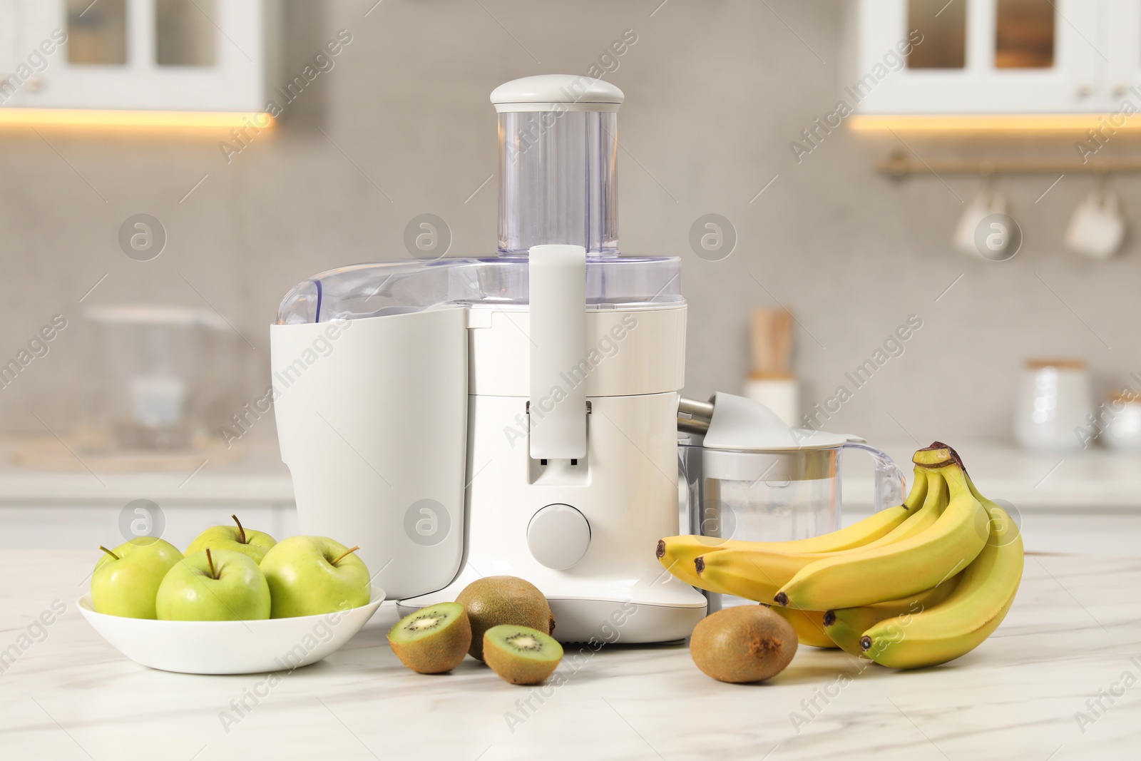 Photo of Modern juicer, apples, kiwi and bananas on white marble table in kitchen