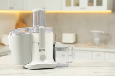 Photo of Modern juicer on white marble table in kitchen, space for text