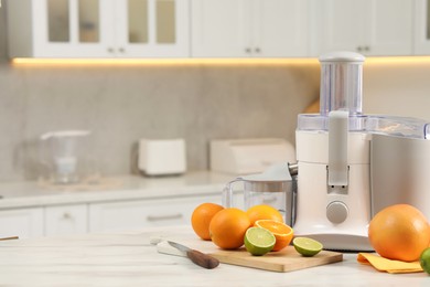 Photo of Modern juicer, oranges and limes on white marble table in kitchen, space for text