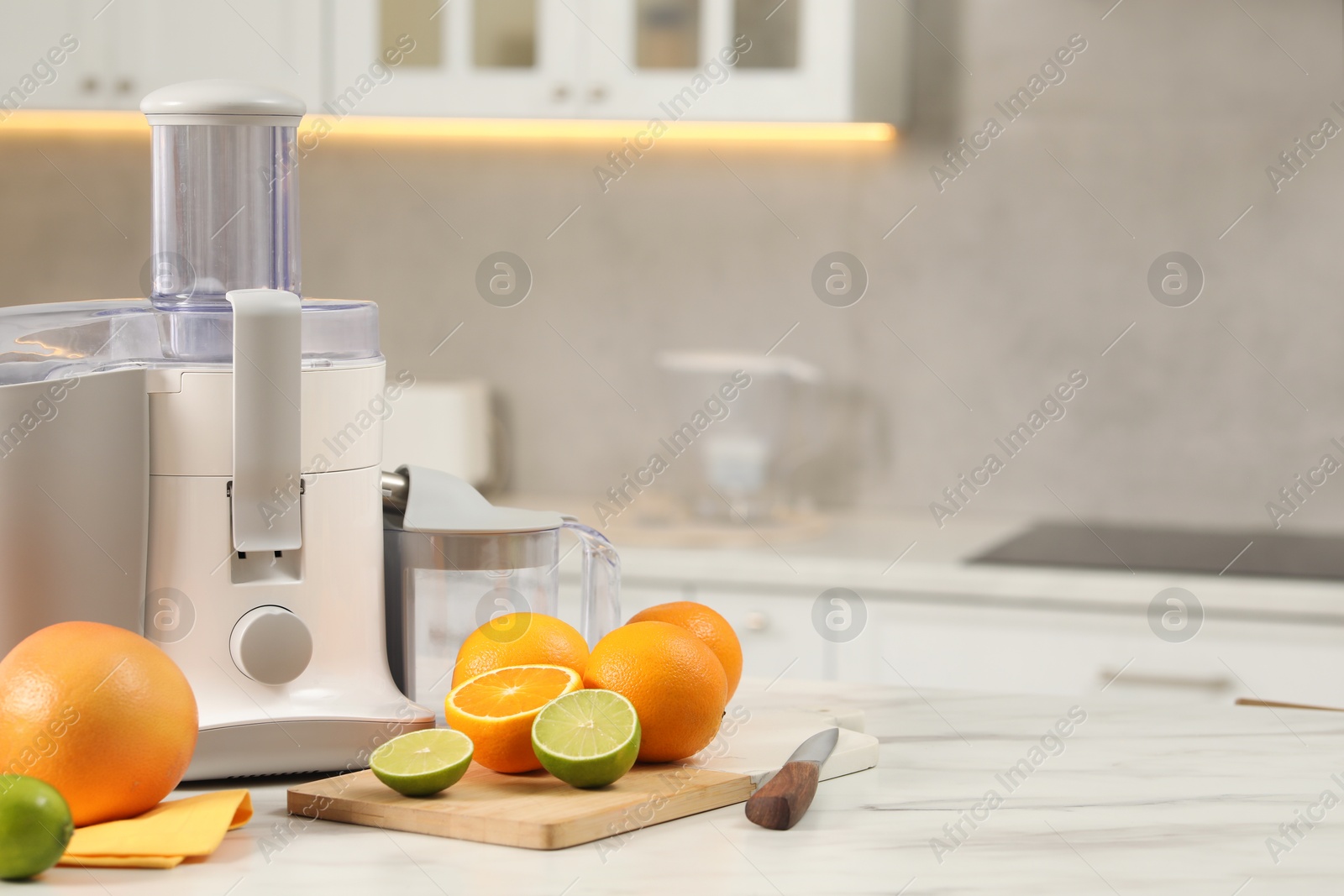 Photo of Modern juicer, oranges and limes on white marble table in kitchen, space for text