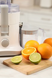 Photo of Modern juicer, oranges and limes on white marble table in kitchen, closeup