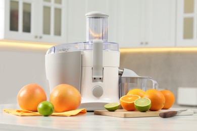 Photo of Modern juicer, oranges and limes on white marble table in kitchen