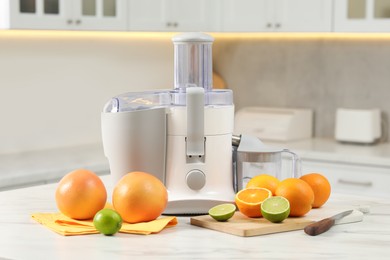 Modern juicer, oranges and limes on white marble table in kitchen