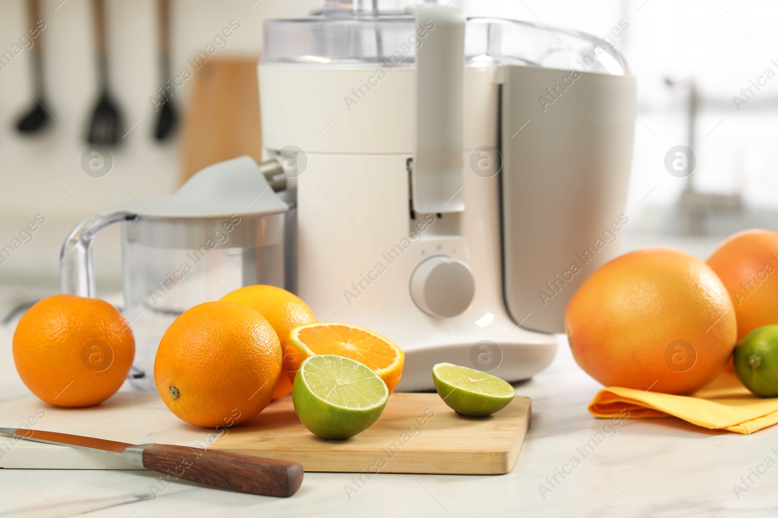 Photo of Modern juicer, oranges and limes on white marble table in kitchen, closeup