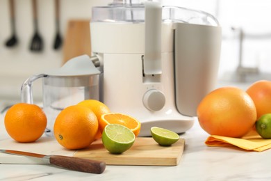 Modern juicer, oranges and limes on white marble table in kitchen, closeup