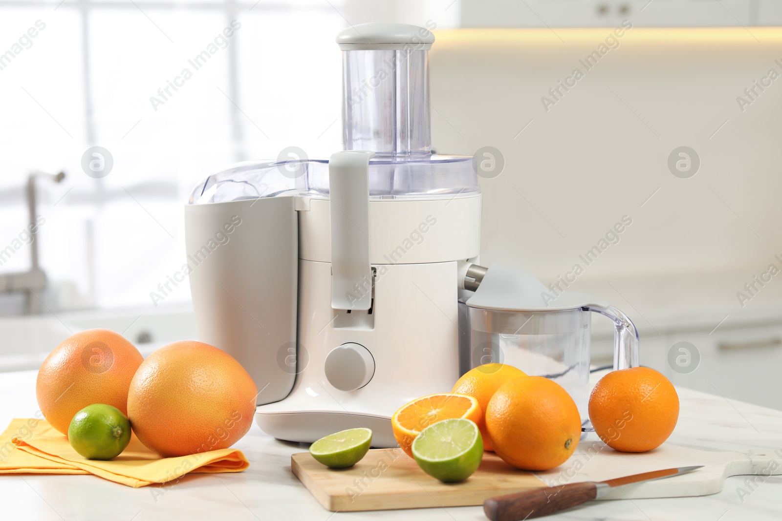 Photo of Modern juicer, oranges and limes on white marble table in kitchen