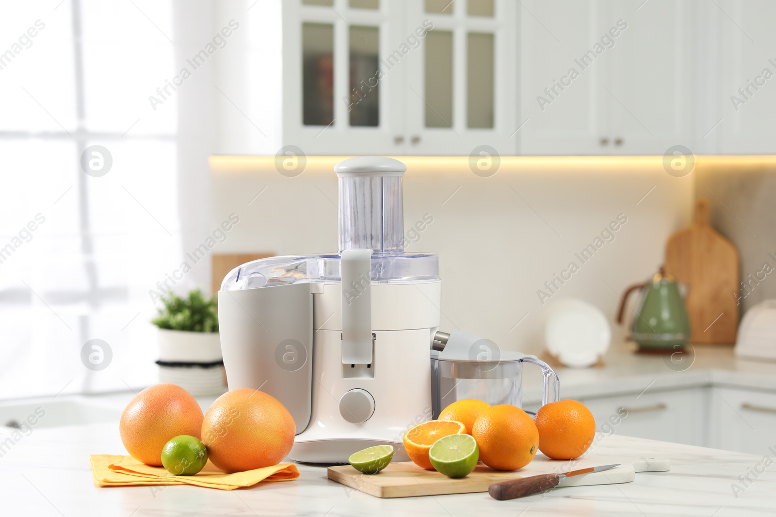 Photo of Modern juicer, oranges and limes on white marble table in kitchen