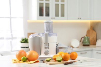 Modern juicer, oranges and limes on white marble table in kitchen