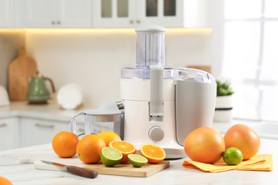 Photo of Modern juicer, oranges and limes on white marble table in kitchen