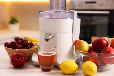 Photo of Modern juicer, fresh fruits and glass on white marble table in kitchen, closeup