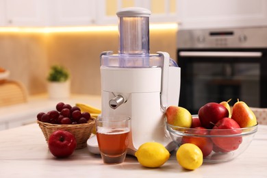 Photo of Modern juicer, fresh fruits and glass on white marble table in kitchen