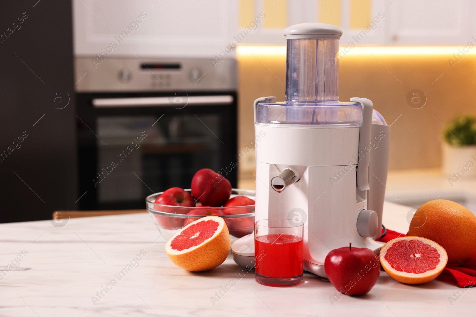 Photo of Modern juicer, fresh fruits and glass on white marble table in kitchen