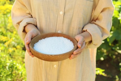 Photo of Woman holding plant fertilizer in bowl outdoors, closeup