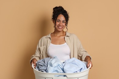 Photo of Happy woman with basket full of laundry on beige background