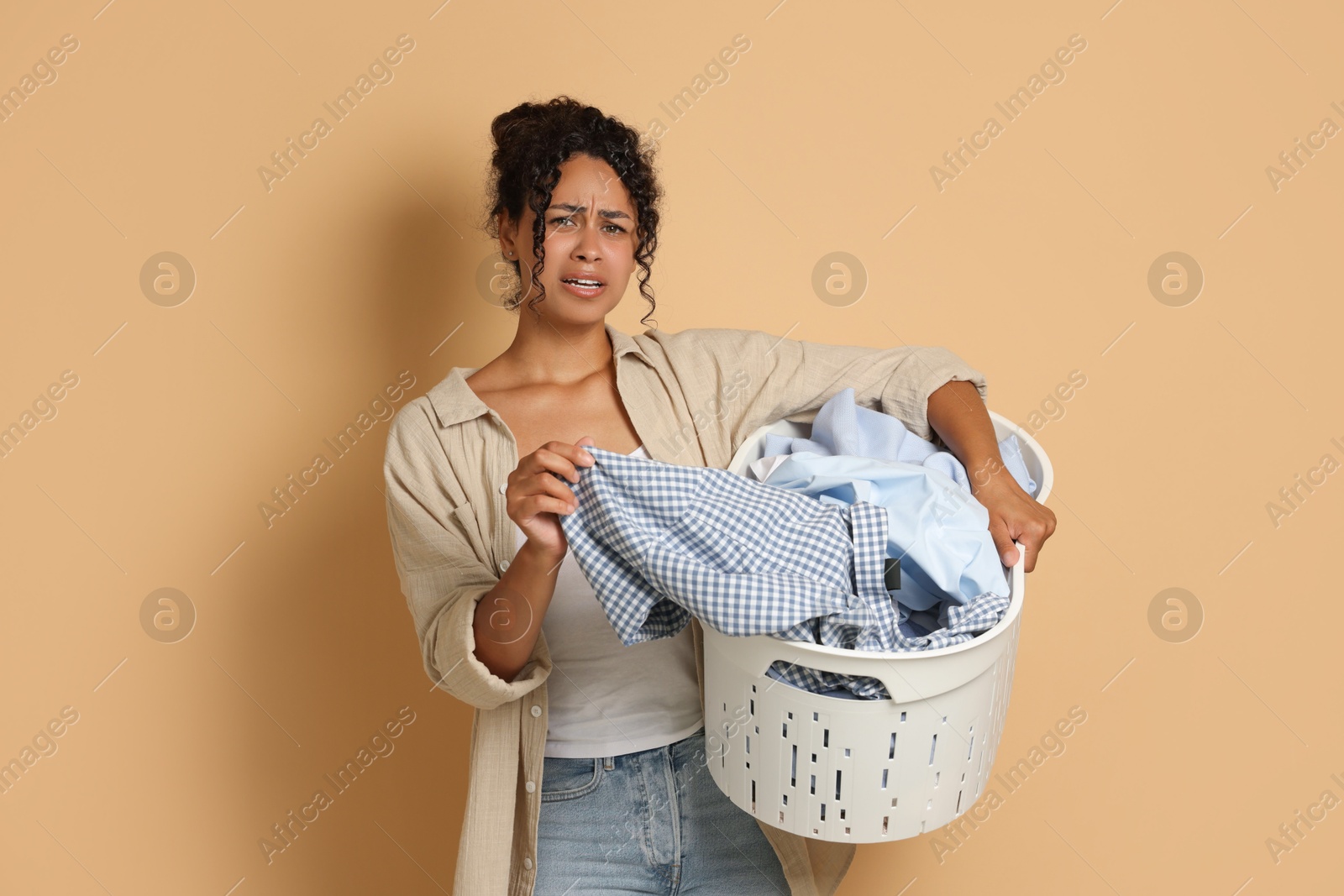 Photo of Displeased woman with basket full of laundry on beige background