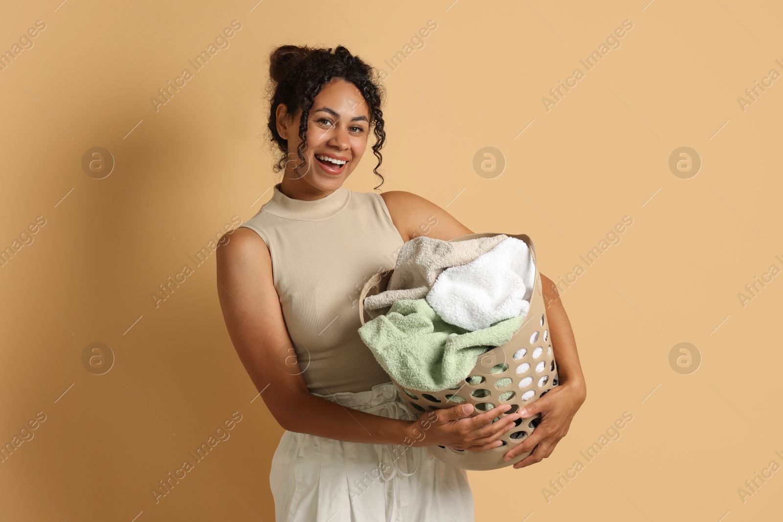 Photo of Happy woman with basket full of laundry on beige background