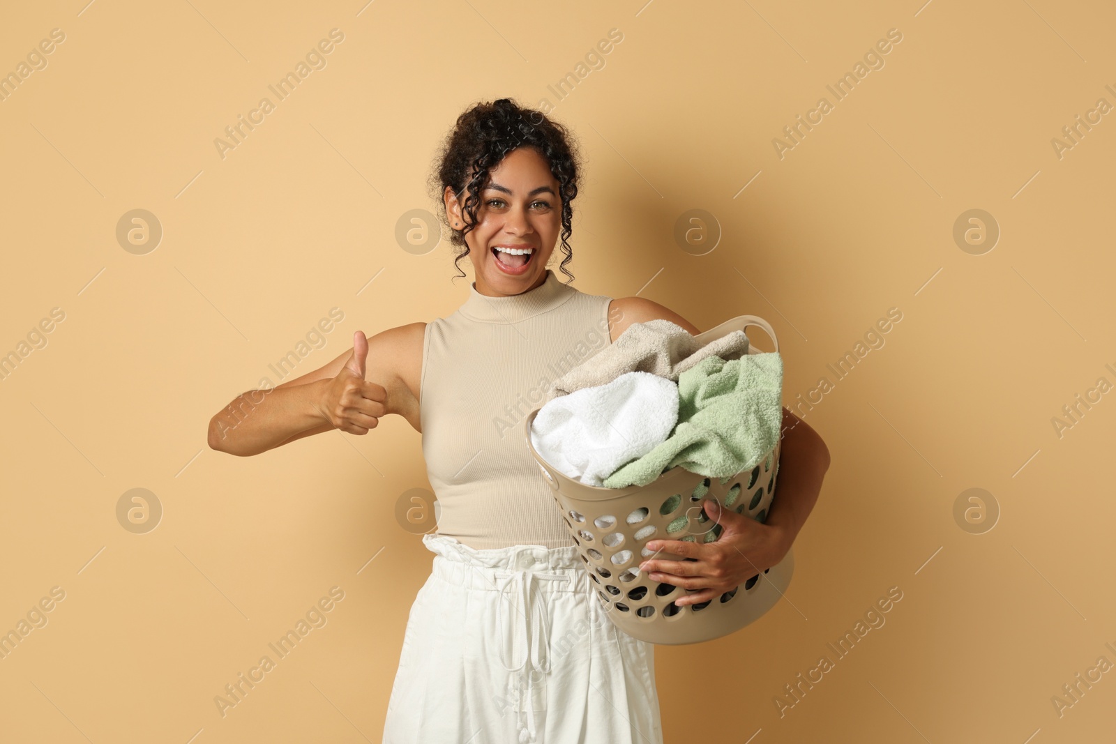 Photo of Happy woman with basket full of laundry on beige background