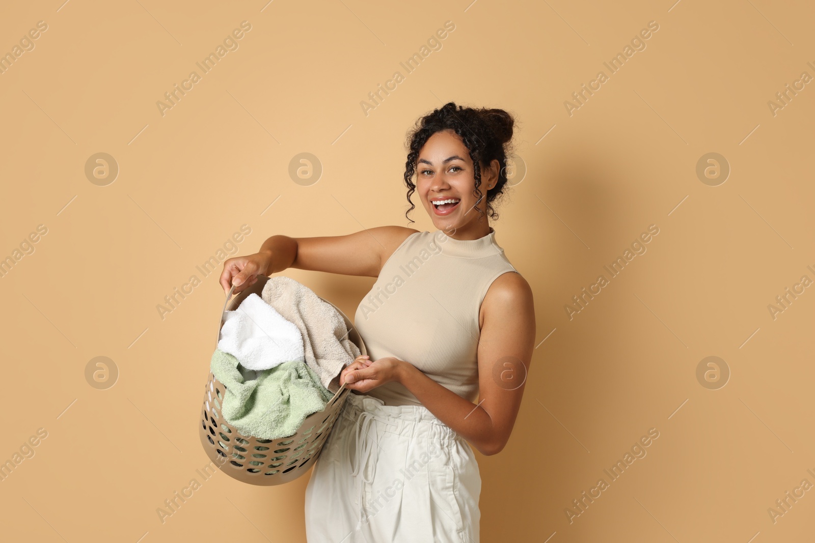 Photo of Happy woman with basket full of laundry on beige background