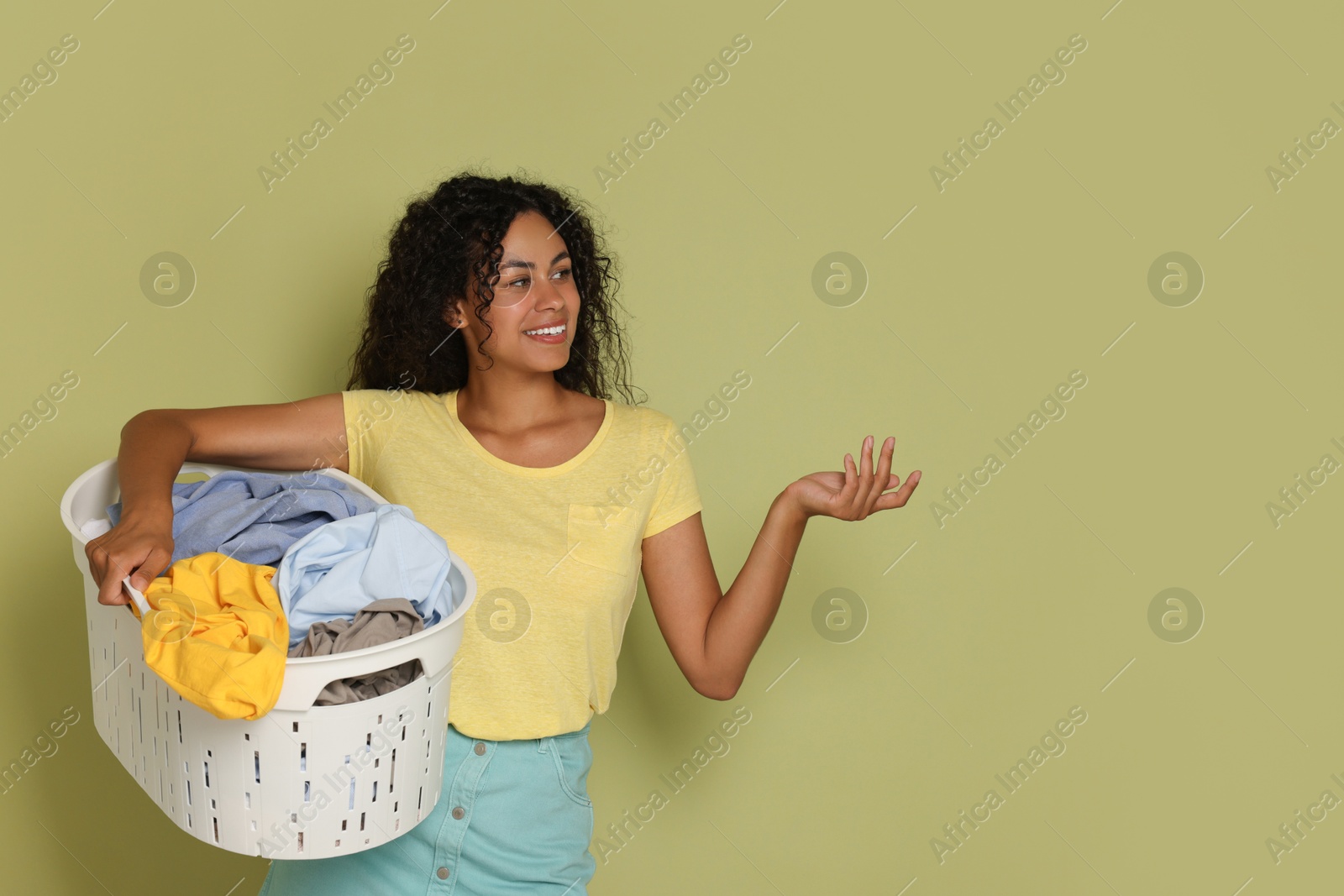 Photo of Happy woman with basket full of laundry on olive background, space for text