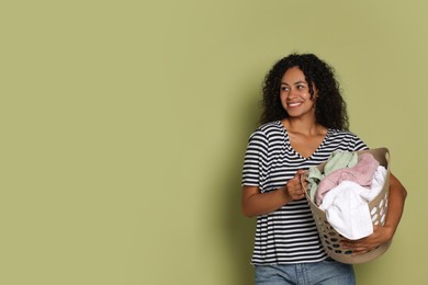 Photo of Happy woman with basket full of laundry on olive background, space for text