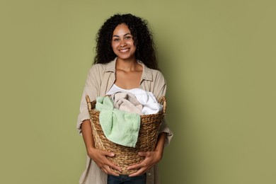 Photo of Happy woman with basket full of laundry on olive background