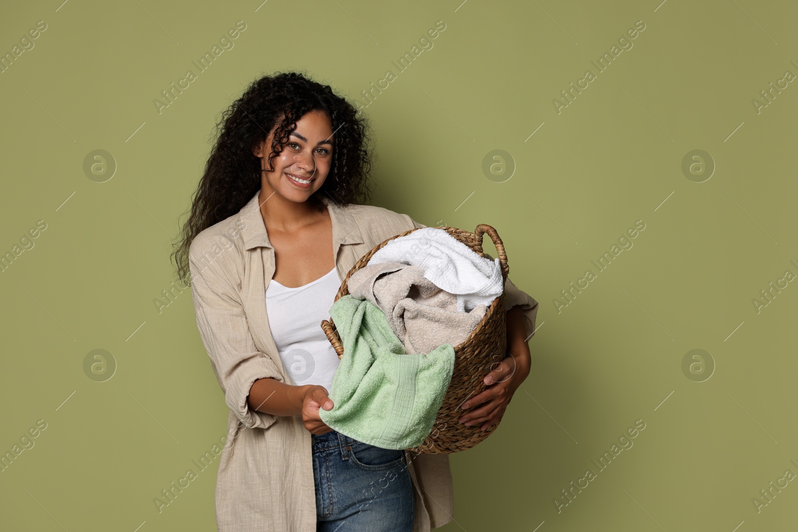 Photo of Happy woman with basket full of laundry on olive background, space for text