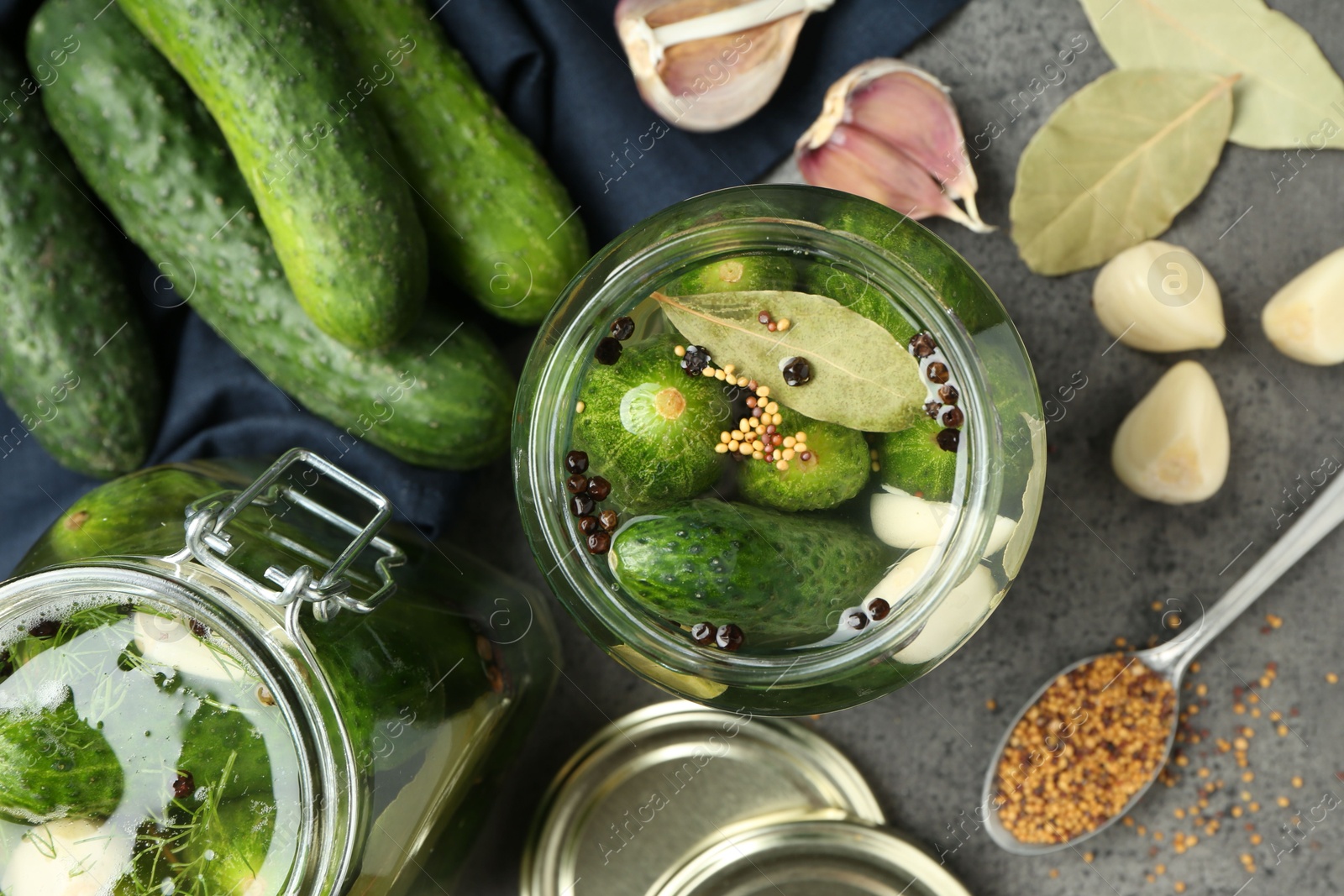 Photo of Making pickles. Fresh cucumbers and spices in jars on grey table, flat lay