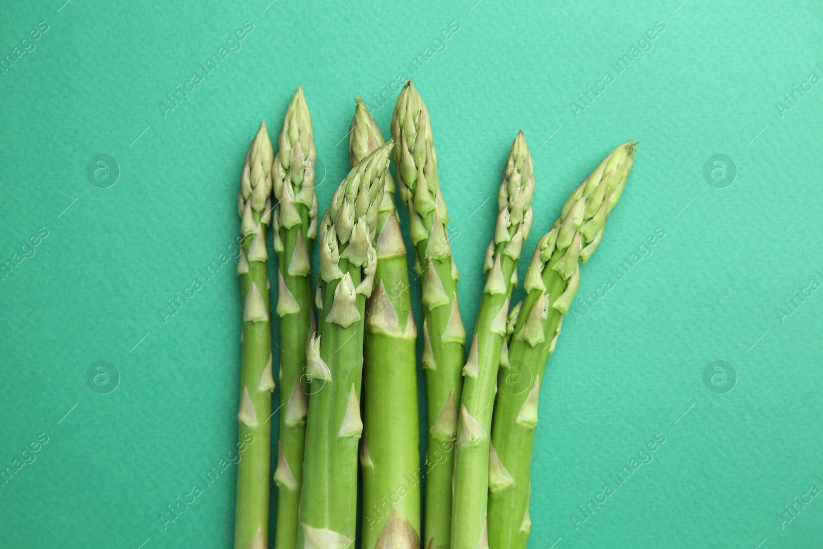 Photo of Fresh green asparagus stems on turquoise table, top view