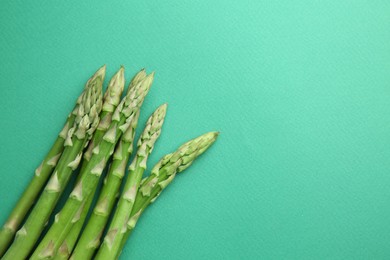 Photo of Fresh green asparagus stems on turquoise table, top view. Space for text