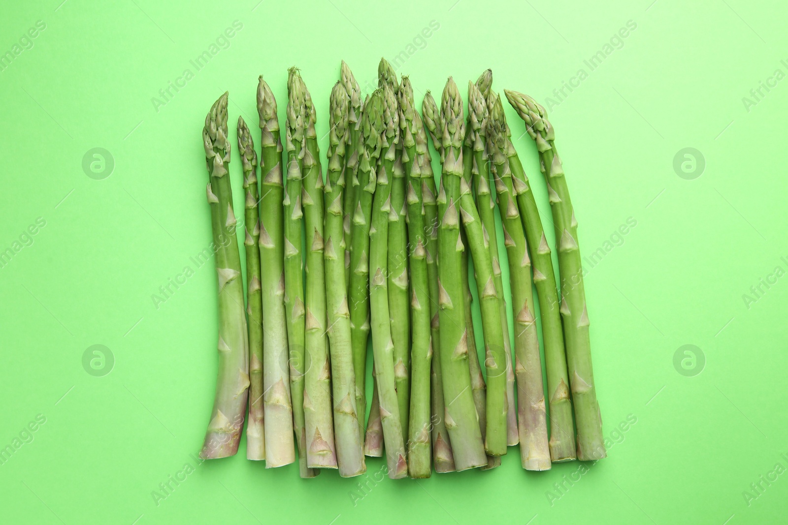 Photo of Fresh asparagus stems on green table, top view