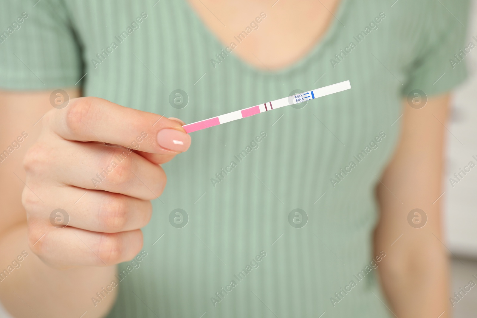 Photo of Woman holding positive pregnancy test indoors, closeup view