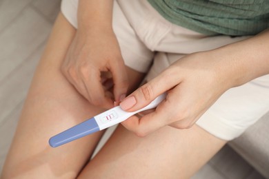 Photo of Woman holding positive pregnancy test indoors, closeup view