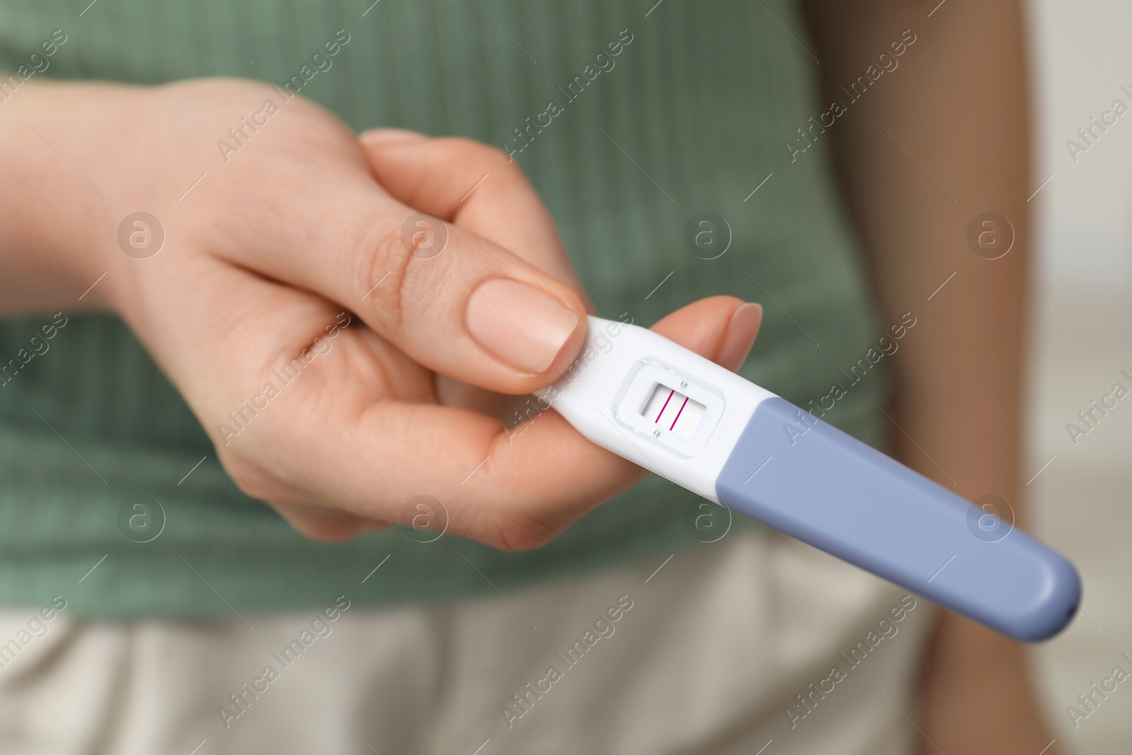 Photo of Woman holding positive pregnancy test indoors, closeup view