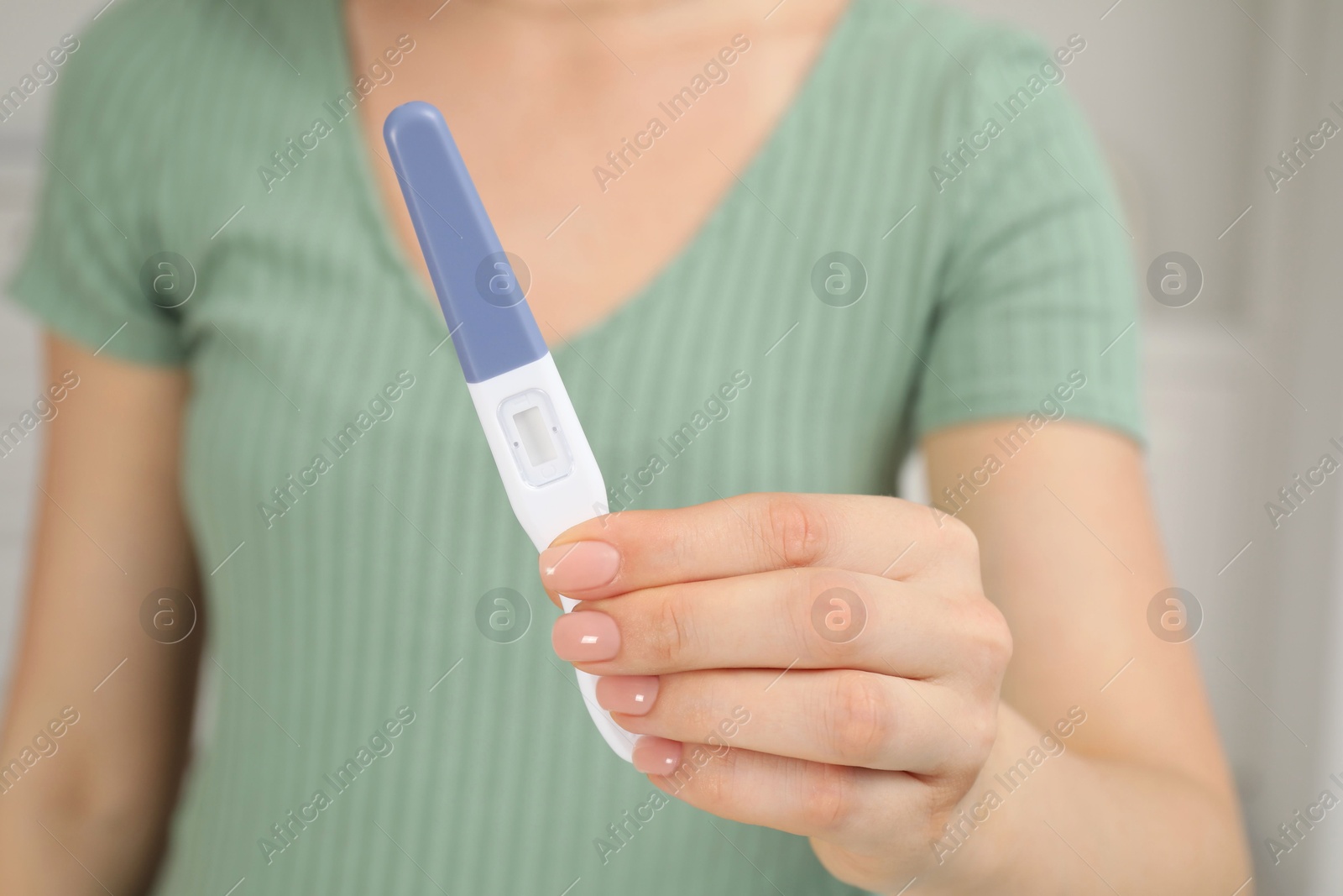 Photo of Woman holding pregnancy test indoors, closeup view