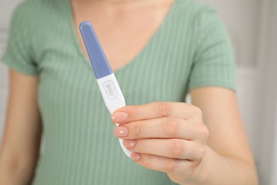 Woman holding pregnancy test indoors, closeup view