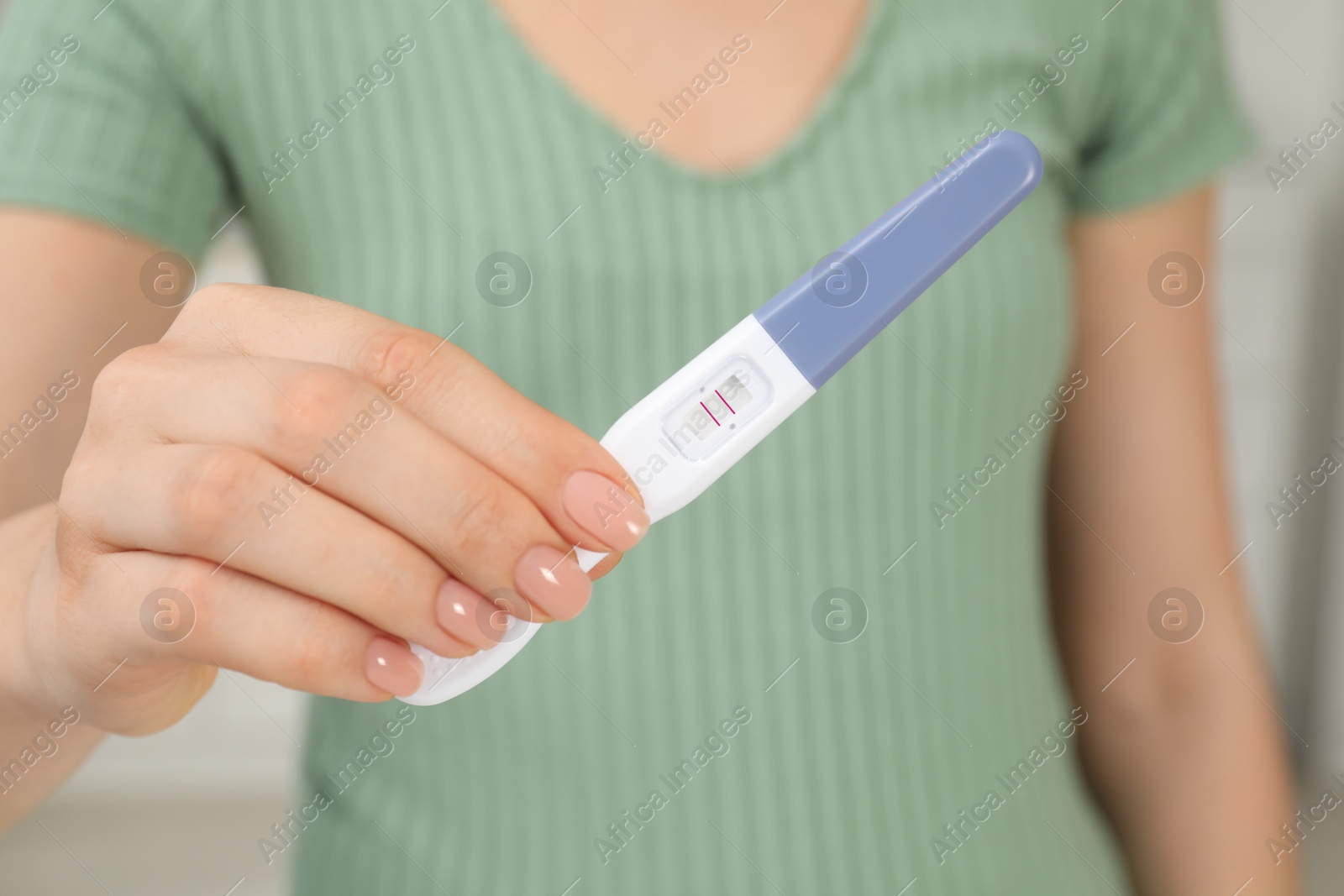 Photo of Woman holding positive pregnancy test indoors, closeup view