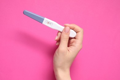 Woman holding pregnancy test on pink background, top view