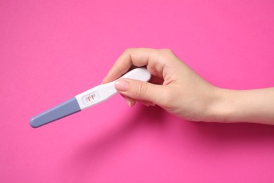 Photo of Woman holding pregnancy test on pink background, top view